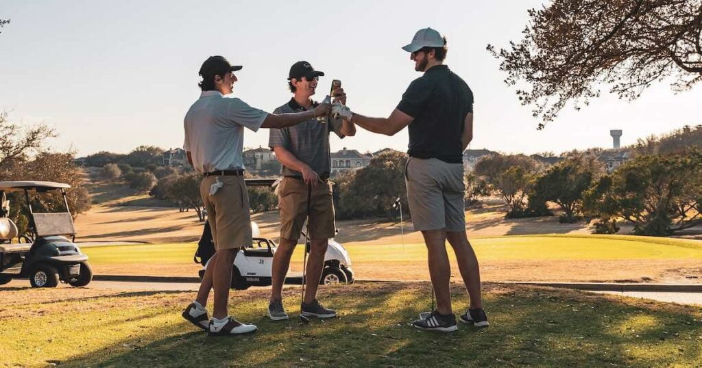 Golfers on the tee box raising drinks to cheers and celebrating a birdie or an eagle.