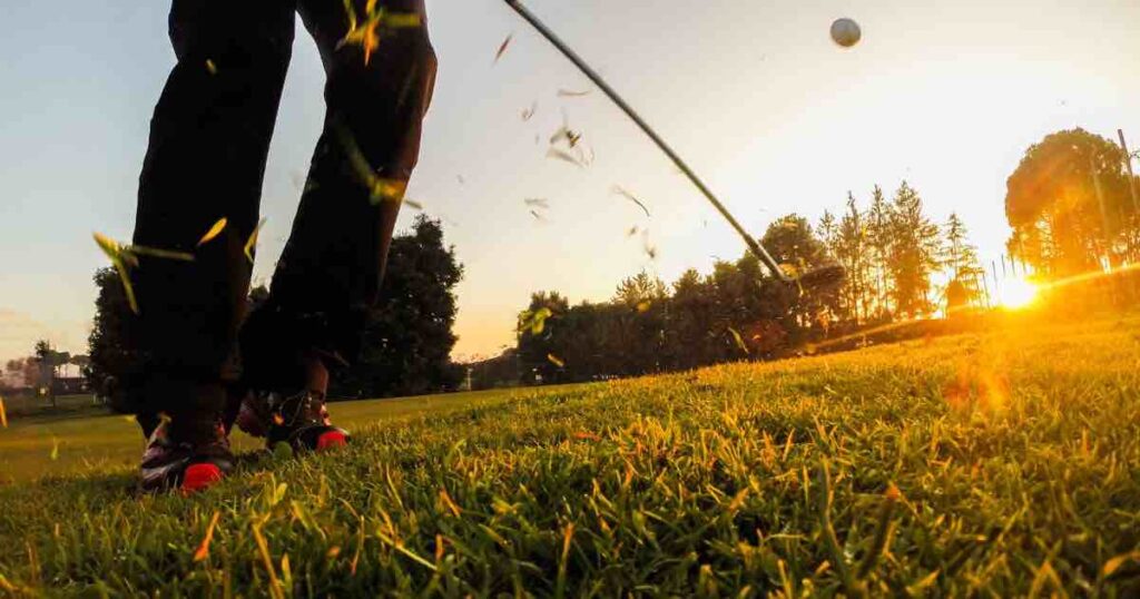 The feet of a golfer at twilight hitting a chip shot and putting backspin on the golf ball