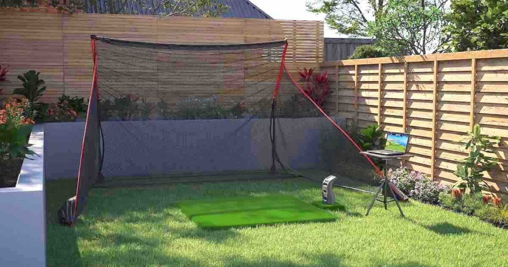 A home golf simulator and launch monitor set up in a backyard with a golf mat and swing net.