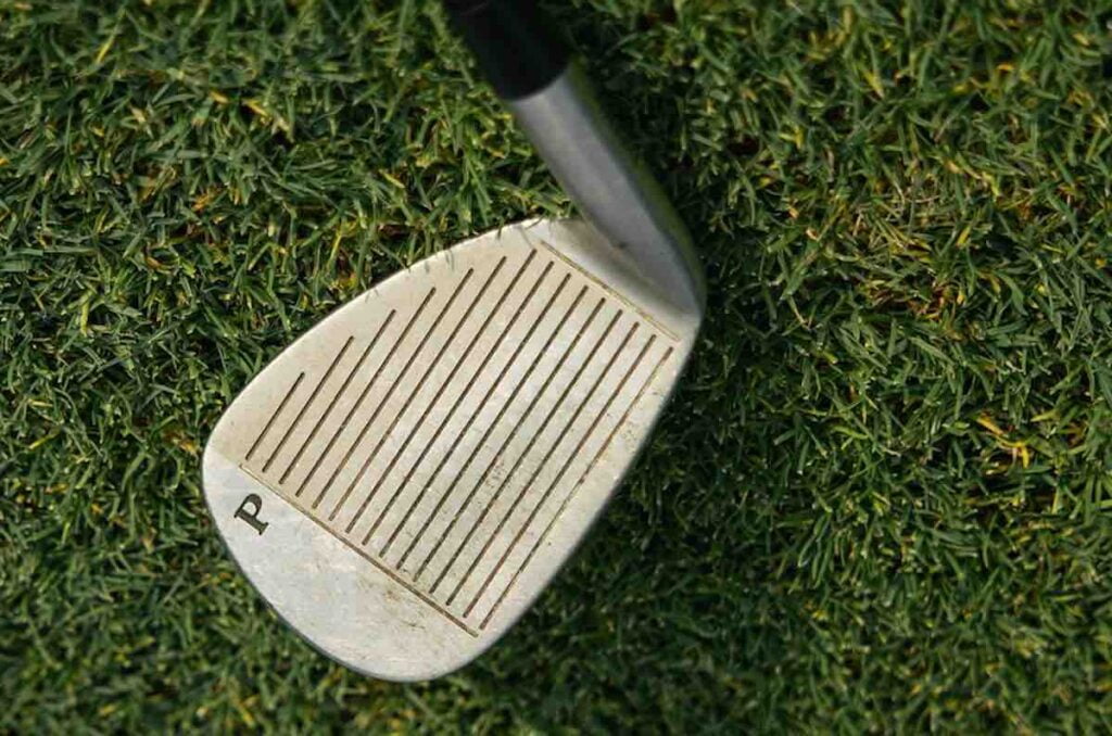 A golf club laying on the grass with dirt in its grooves, that should be clean for better performance