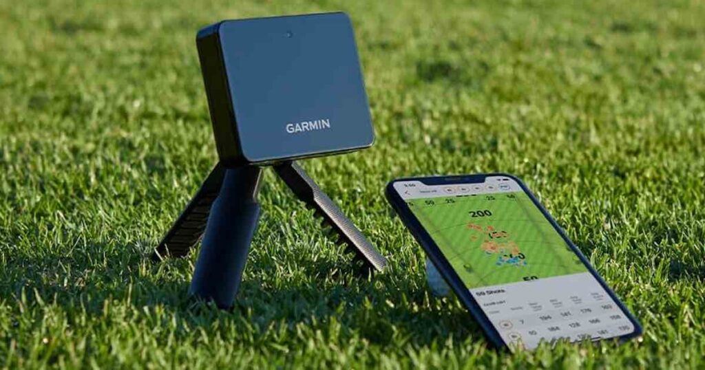 The Garmin Approach R10 Launch monitor and a smart phone showing the Garmin Golf App sitting on the grass at a golf course.