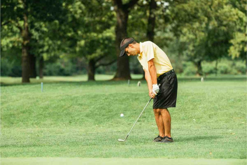 A golfer in a yellow shirt and black shorts putting backspin on the golf ball during a chip shot on to the green