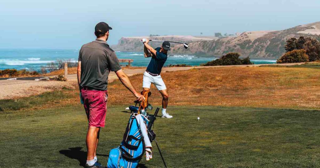 two golfers of differing skill levels teeing off at an ocean front golf course. They can compete against each other thanks to the golf handicap system.