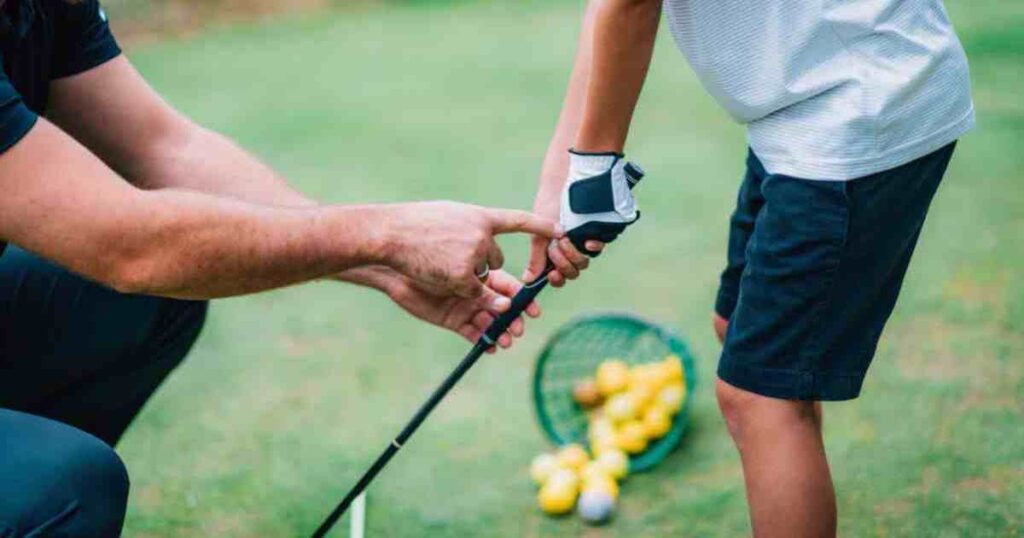 male golf instructor showing boy how to hold a golf club