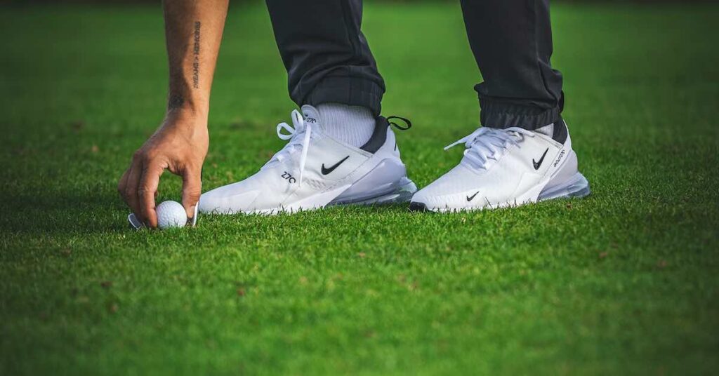 golf wearing comfortable white golf shoes picking up ball.