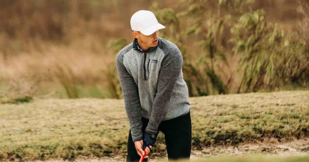 man in white hat and grey vest in a golf stance.