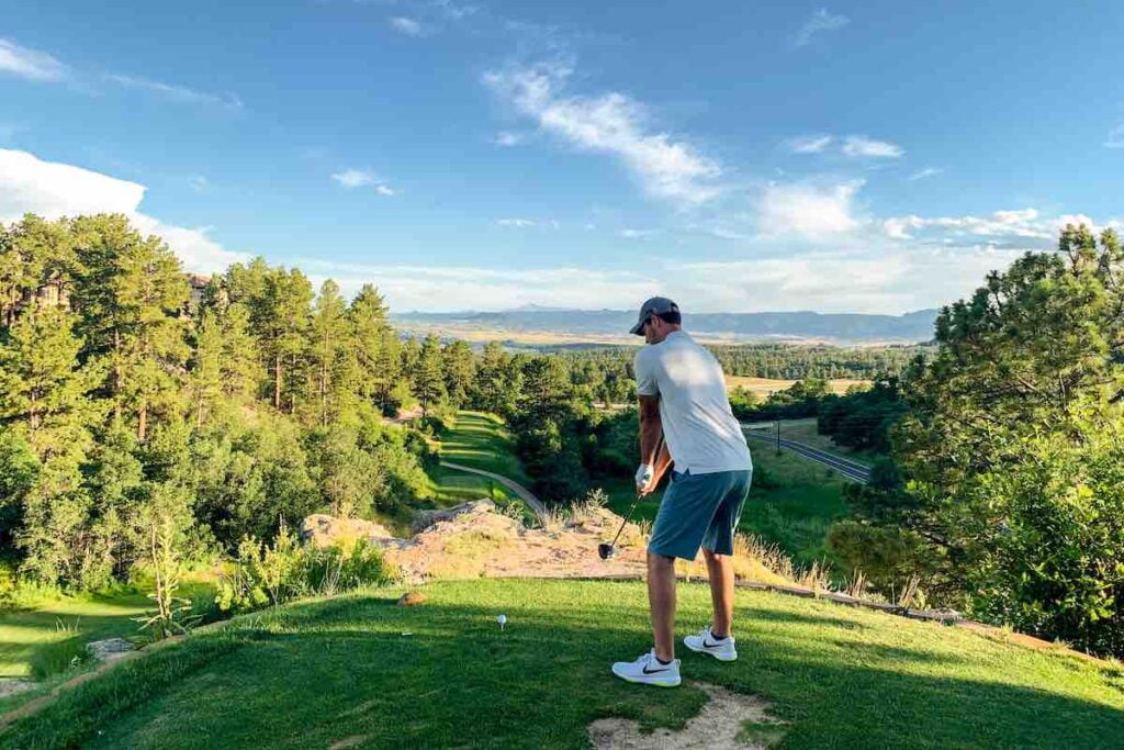 Man in white shirt in a golf stance swinging a driver