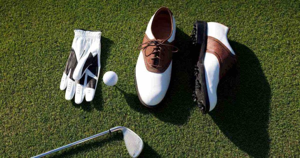 golf shoes, glove, golf ball and iron laid out on the grass.