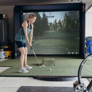 Female golfer hitting a golf bal with an iron on a SwingBay golf simulator screen and enclosure
